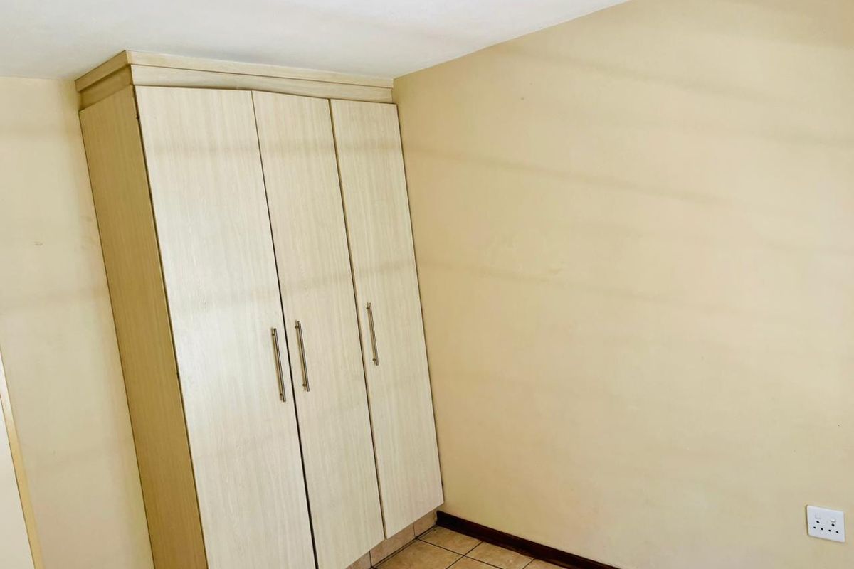 A simple bedroom featuring light-toned built-in wardrobes, tiled flooring, and neutral wall finishes, providing a clean and functional space.
