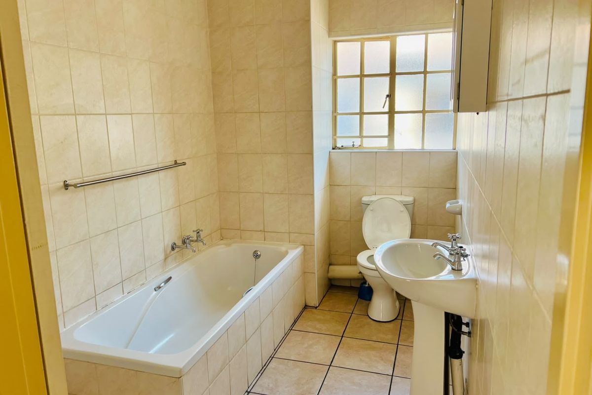 A functional bathroom featuring a bathtub, pedestal basin, and toilet with neutral wall and floor tiling.