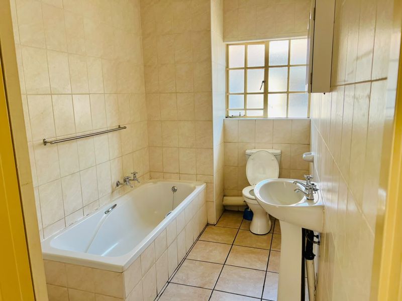 A functional bathroom featuring a bathtub, pedestal basin, and toilet with neutral wall and floor tiling.