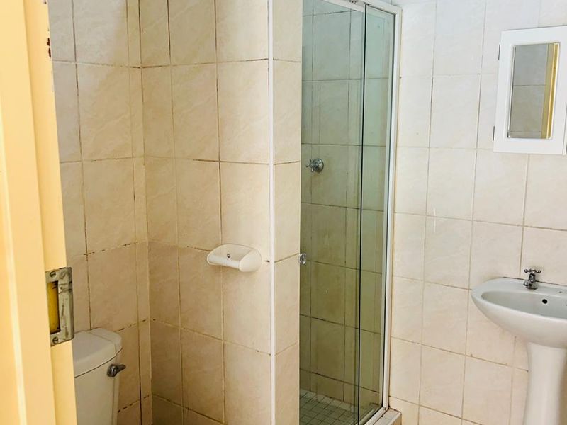 A functional bathroom featuring a shower enclosure, pedestal sink, and toilet with neutral wall and floor tiling.