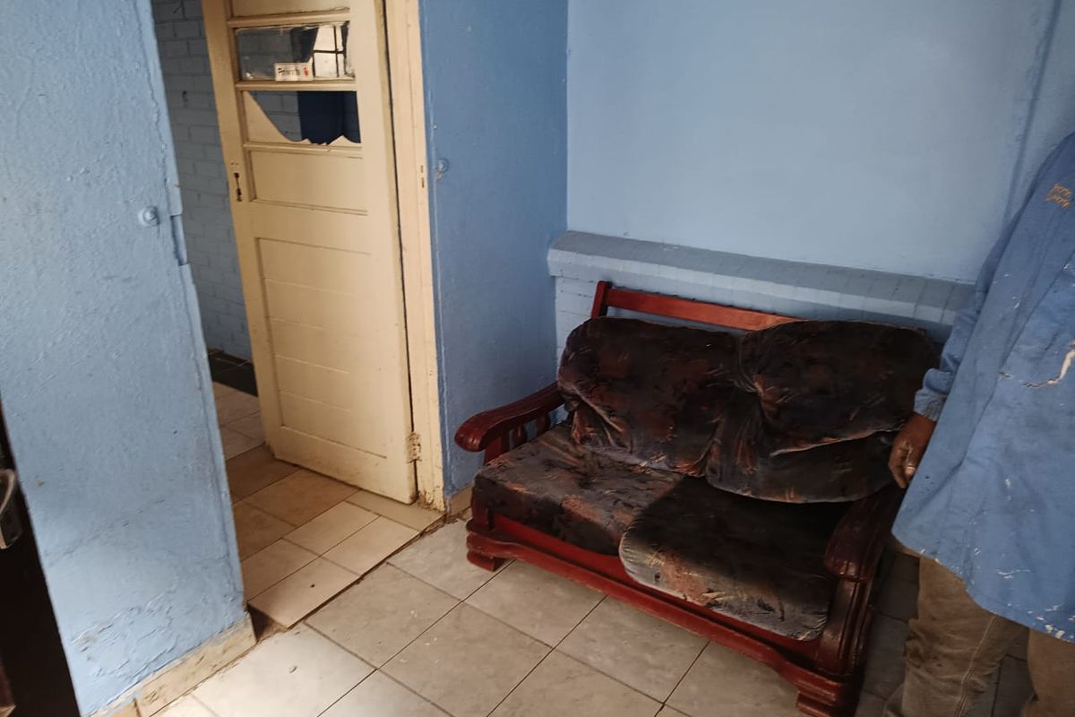A small living area featuring tiled flooring and a traditional timber door, currently requiring significant cosmetic updates and wall repairs.
