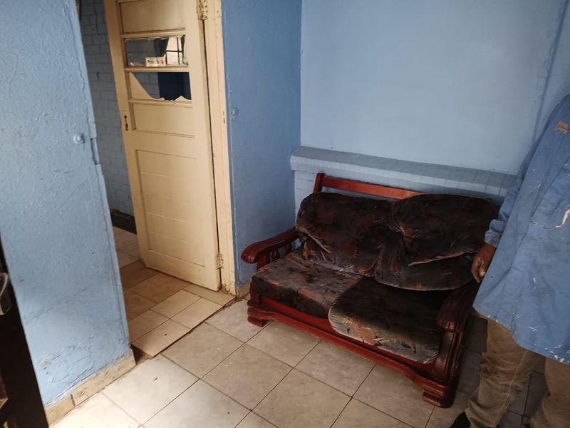 A small living area featuring tiled flooring and a traditional timber door, currently requiring significant cosmetic updates and wall repairs.
