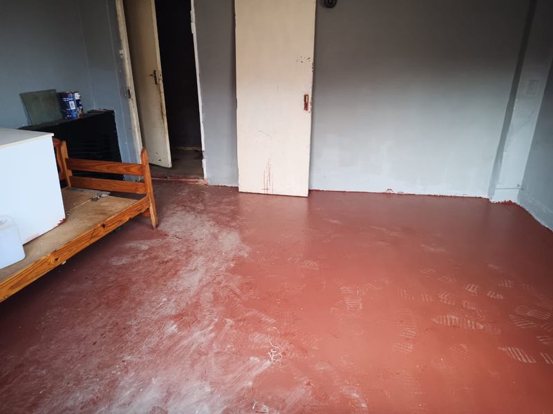 An empty bedroom featuring a painted concrete floor and internal doors, requiring cosmetic updates and finishing to improve its overall condition.