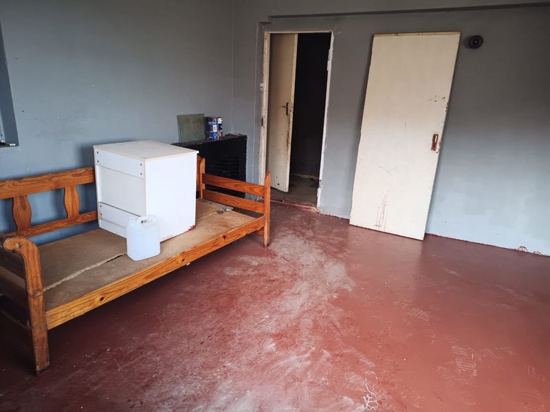 A vacant bedroom featuring painted concrete flooring and basic interior doors, requiring cosmetic updates and finishing touches to improve its overall condition.
