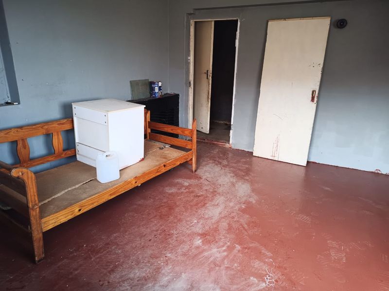 A sparse bedroom featuring painted concrete flooring and grey walls, currently in need of cosmetic refurbishment and finishing touches.