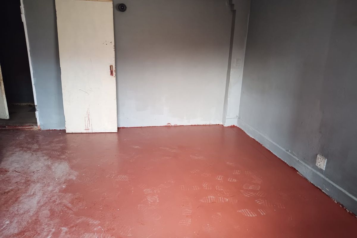 An empty bedroom featuring painted concrete flooring and grey walls, currently requiring cosmetic updates and finishing touches to improve its overall condition.