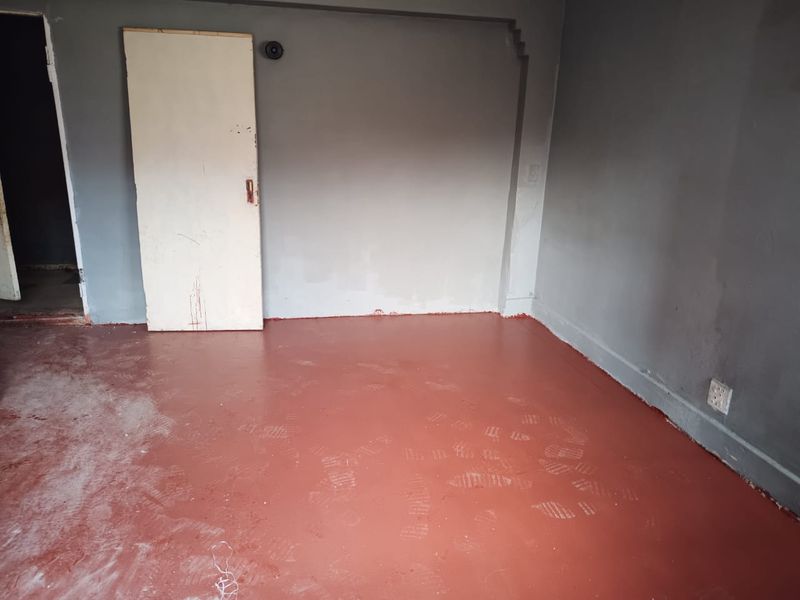 An empty bedroom featuring painted concrete flooring and grey walls, currently requiring cosmetic updates and finishing touches to improve its overall condition.