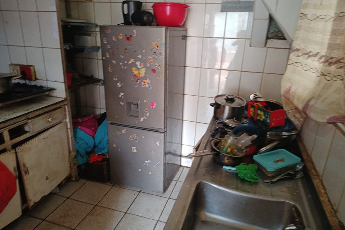 A dated kitchen featuring tiled walls and flooring, stainless steel sink, and built-in cabinetry in need of renovation.