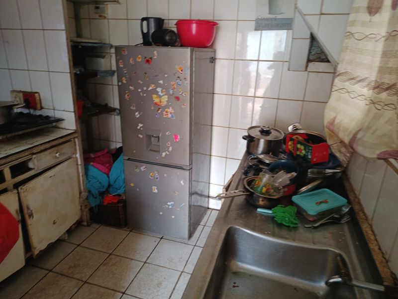 A dated kitchen featuring tiled walls and flooring, stainless steel sink, and built-in cabinetry in need of renovation.