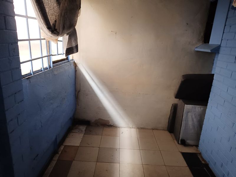 A small utility space featuring painted brick walls, security bars on the window, and tiled flooring, currently in need of maintenance and cosmetic updates.
