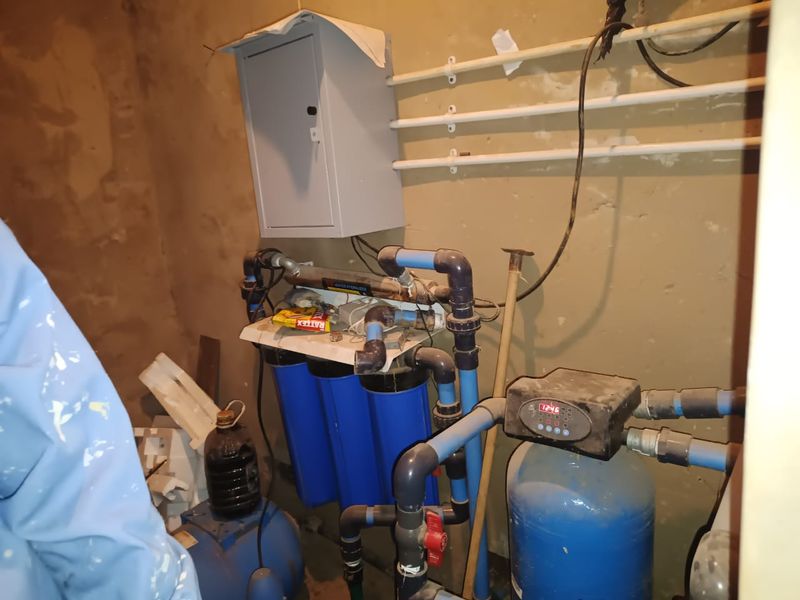 Utility space featuring a water filtration system, pressure pump, and electrical distribution board with exposed plumbing and unfinished wall surfaces.