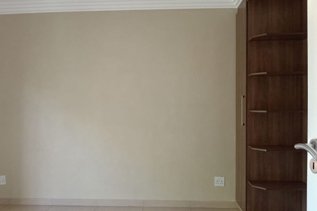 A clean, empty bedroom featuring neutral walls, crown molding, and a built-in wooden cupboard with open shelving.