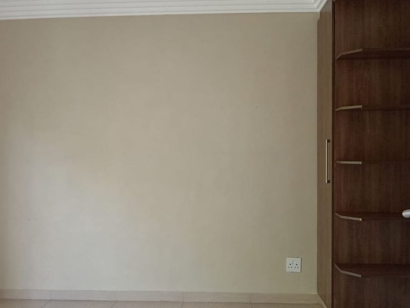 A clean, empty bedroom featuring neutral walls, crown molding, and a built-in wooden cupboard with open shelving.