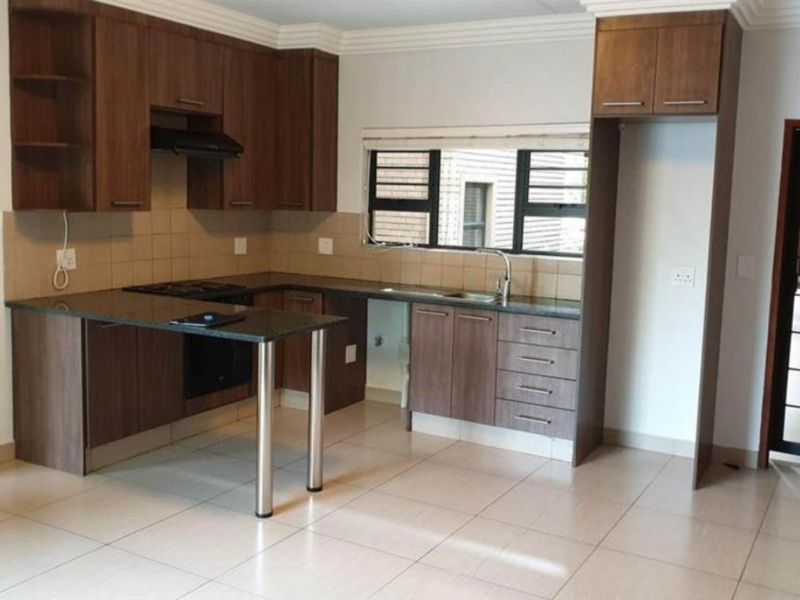 A functional kitchen featuring dark wood cabinetry, granite countertops, a breakfast nook, and integrated appliances, set against a neutral tiled floor.
