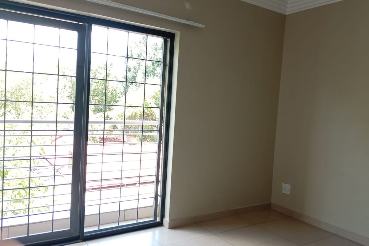 An empty living room featuring tiled flooring and a large sliding glass door with integrated security bars, providing access to an outdoor area.