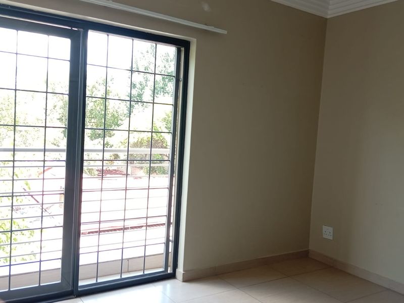 An empty living room featuring tiled flooring and a large sliding glass door with integrated security bars, providing access to an outdoor area.