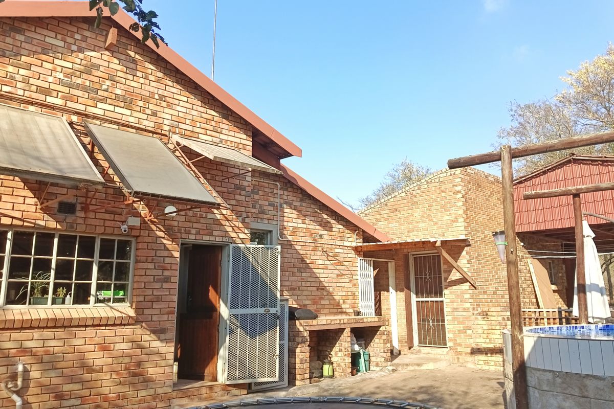 Rear exterior view of a face brick house featuring solar water heating panels, a built-in brick braai area, and access to the pool.