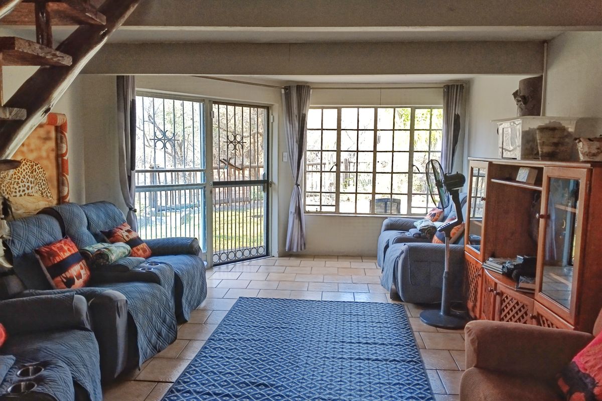 A living room featuring tiled flooring, exposed ceiling beams, and a timber staircase, with direct access to the garden through a security gate.