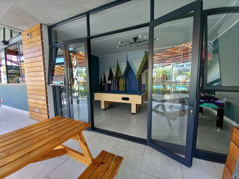 A modern clubhouse area featuring large glass doors, tiled flooring, and timber wall accents, providing a bright and inviting communal space.