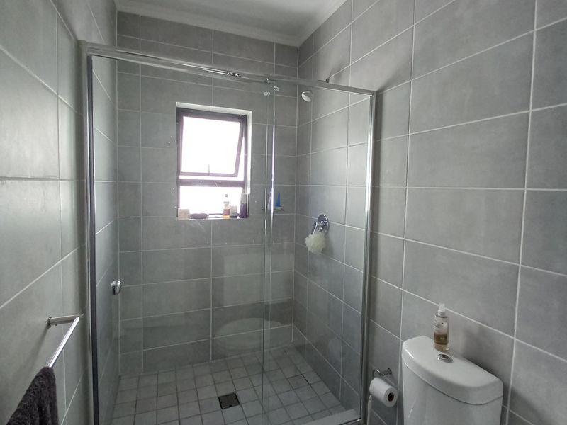 A modern bathroom featuring grey wall and floor tiles, a glass-enclosed shower, and a standard toilet.