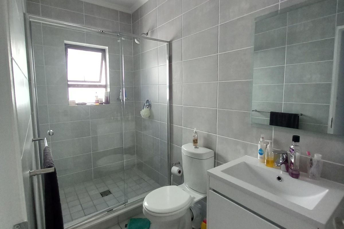 A modern, well-maintained bathroom featuring a glass-enclosed shower, a sleek wall-mounted vanity with a basin, and neutral grey wall and floor tiling.