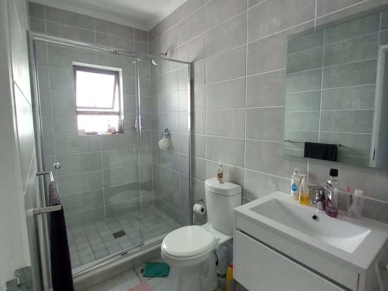 A modern, well-maintained bathroom featuring a glass-enclosed shower, a sleek wall-mounted vanity with a basin, and neutral grey wall and floor tiling.