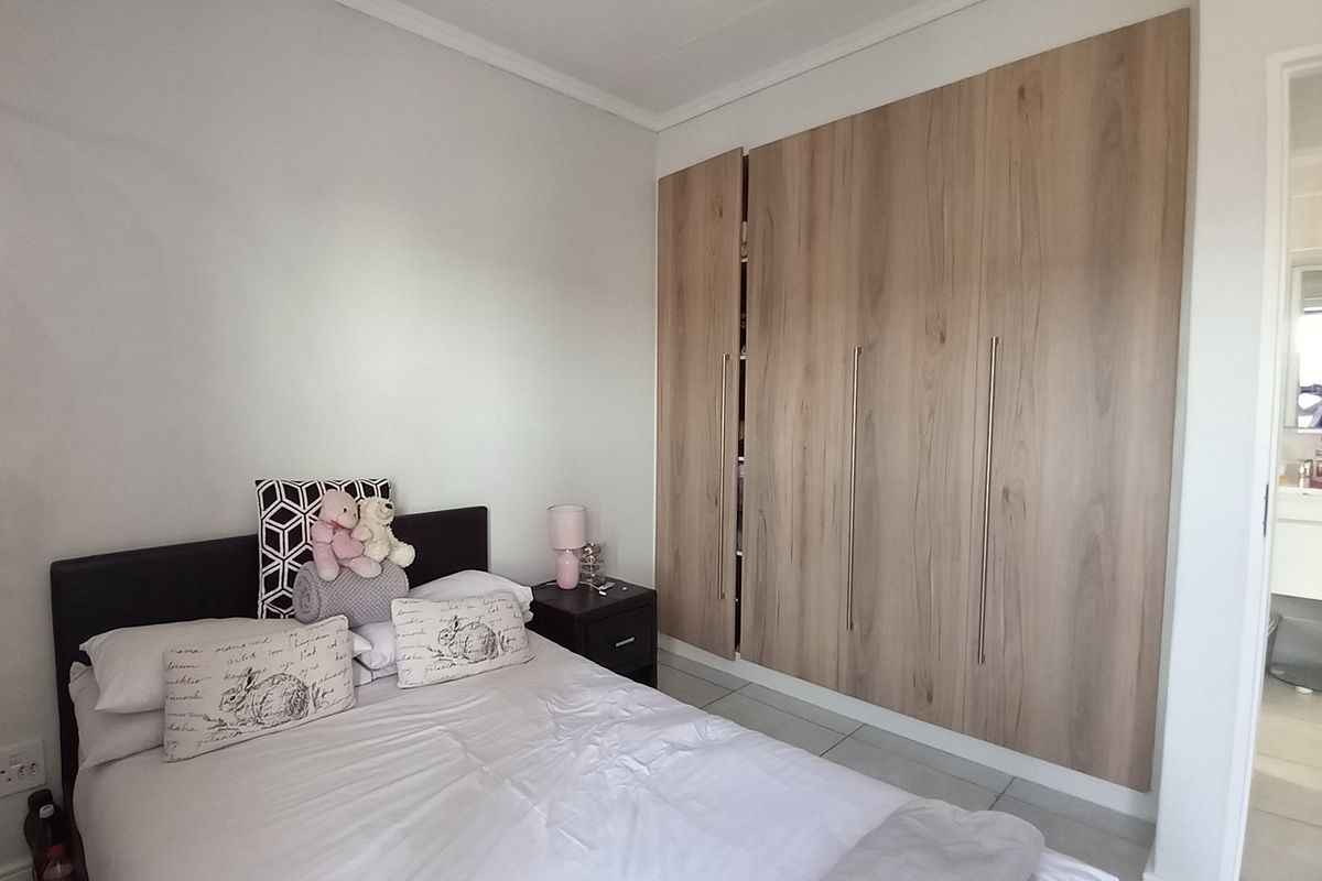 A well-maintained bedroom featuring modern wood-finish built-in cupboards and neutral tiled flooring, offering a clean and functional living space.