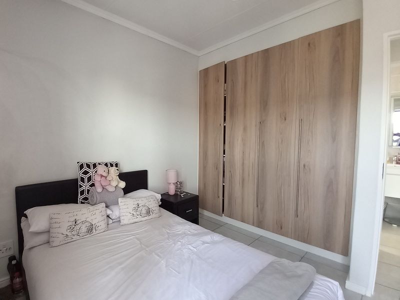 A well-maintained bedroom featuring modern wood-finish built-in cupboards and neutral tiled flooring, offering a clean and functional living space.