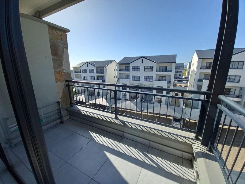 A clean, tiled balcony featuring a metal balustrade and stone cladding detail, offering an open view of the surrounding apartment complex.