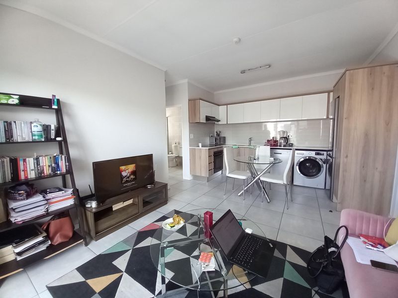 Open-plan living area featuring a modern kitchen with built-in cabinetry, integrated appliances, and tiled flooring, seamlessly connecting to the lounge space.
