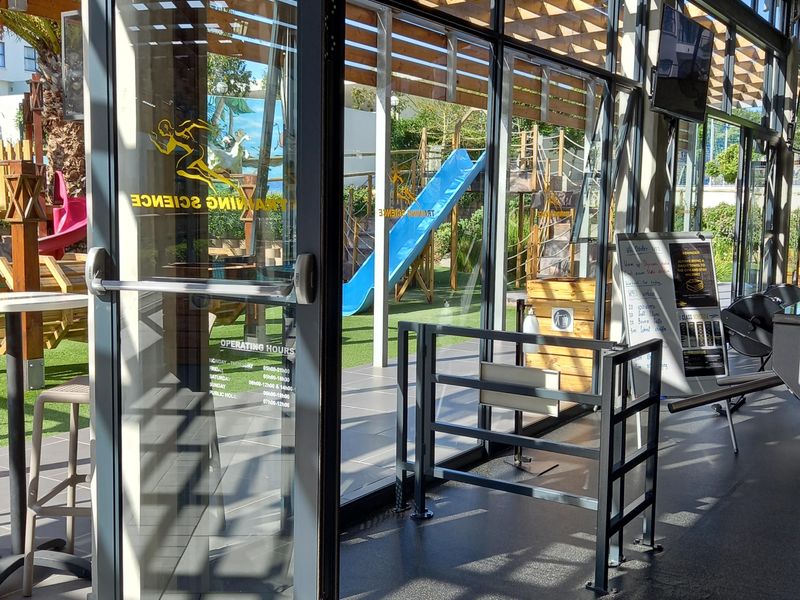 Interior view of a gym facility featuring large glass doors opening to an outdoor play area with a timber pergola structure.