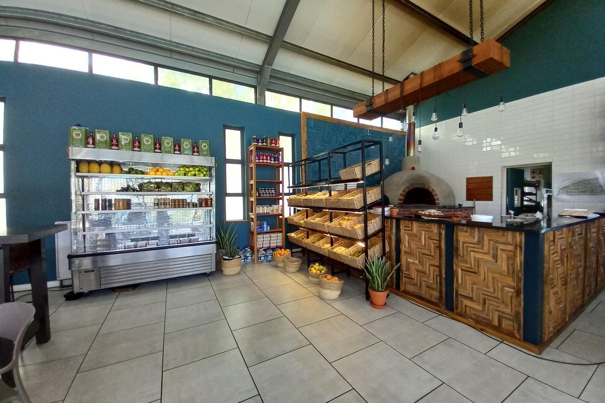 A commercial-style kitchen area featuring a built-in pizza oven, tiled flooring, subway tile backsplash, and exposed industrial roof trusses.