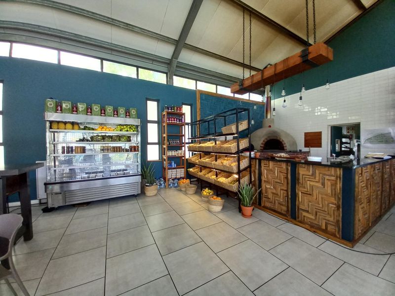 A commercial-style kitchen area featuring a built-in pizza oven, tiled flooring, subway tile backsplash, and exposed industrial roof trusses.