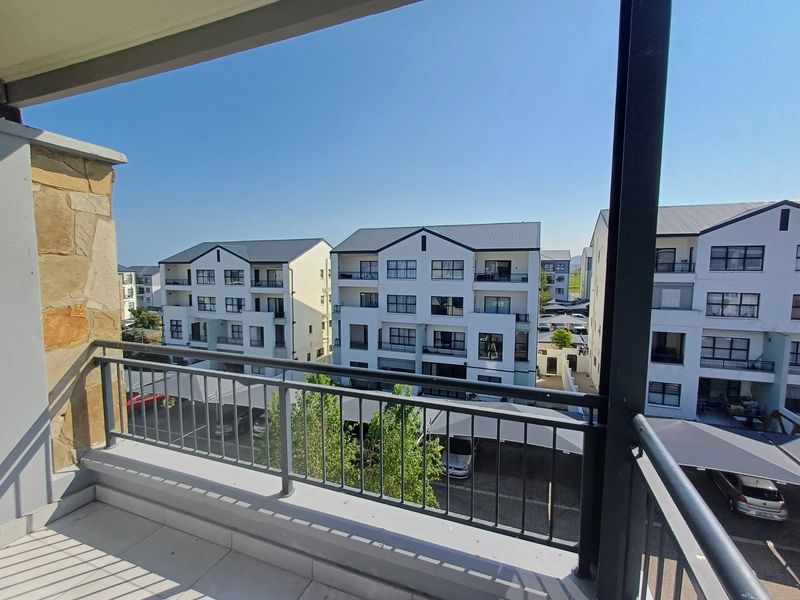 A clean, modern balcony with tiled flooring, metal railings, and stone feature wall, offering an elevated view of the surrounding apartment complex.