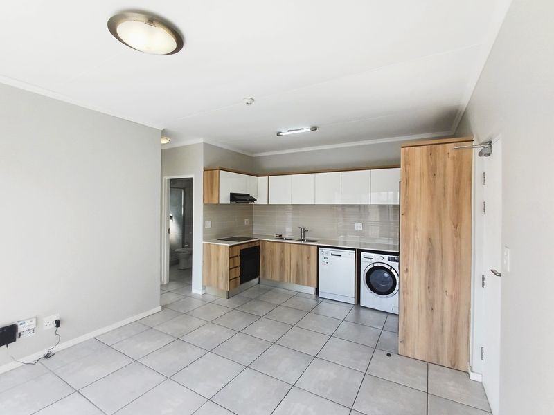 An open-plan kitchen area featuring modern wood-finish cabinetry, tiled flooring, and integrated appliances, providing a clean and functional living space.