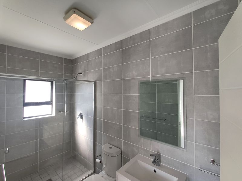 Modern bathroom featuring grey wall tiles, a glass shower enclosure, a vanity basin, and a wall-mounted mirror.