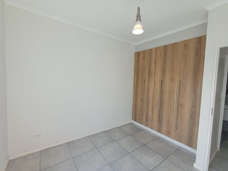 A clean, empty bedroom featuring modern wood-finish built-in cupboards and neutral tiled flooring, providing a versatile space ready for personalization.