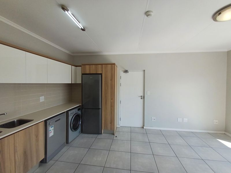 A modern open-plan kitchen area featuring neutral cabinetry, tiled flooring, and integrated appliance spaces, offering a clean and functional layout.