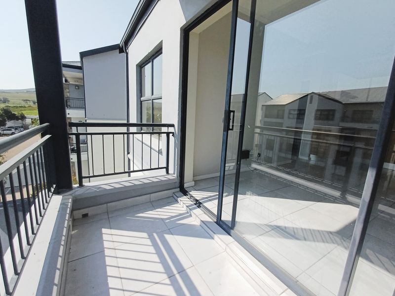 A clean, modern balcony featuring tiled flooring, a metal balustrade, and large sliding glass doors providing access to the interior.