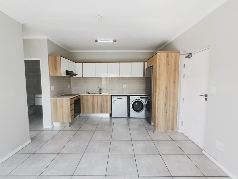 Modern open-plan kitchen featuring light wood-grain cabinetry, white upper cabinets, tiled flooring, and integrated appliance spaces in a clean, well-maintained apartment.