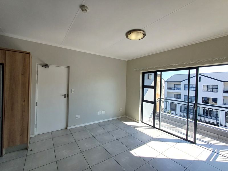 A bright, empty living area featuring neutral tiled flooring, a built-in cupboard, and a large sliding glass door leading to a balcony.