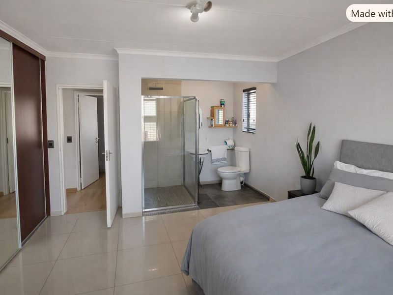 Spacious bedroom featuring an open-plan en-suite bathroom with a glass-enclosed shower, toilet, and built-in wardrobe storage.