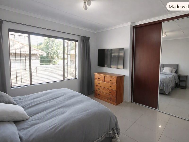 A well-maintained bedroom featuring tiled flooring, a large built-in wardrobe with mirrored doors, and security bars on the window.