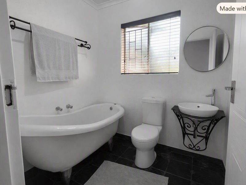 A clean bathroom featuring a classic freestanding bathtub, a modern vessel sink with wall-mounted tap, and dark floor tiling.