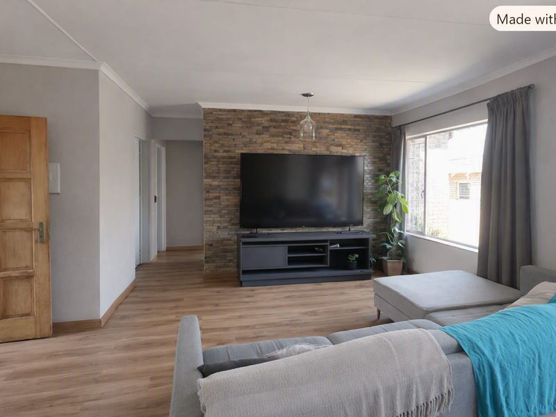 A well-maintained living room featuring a textured stone accent wall, modern laminate flooring, and natural light from a large window.