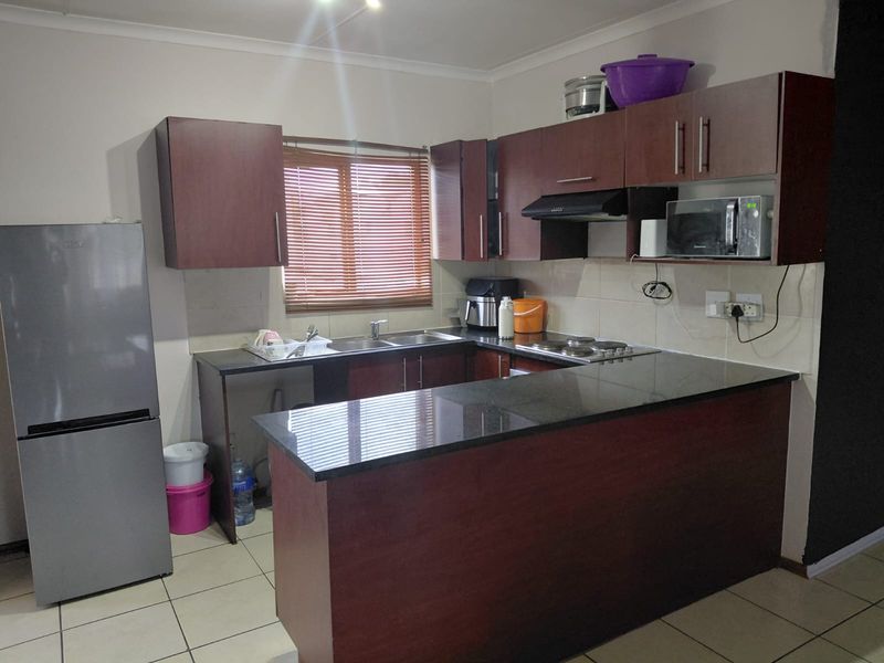 A functional kitchen featuring dark wood cabinetry, granite countertops, an electric hob with extractor fan, and tiled flooring.