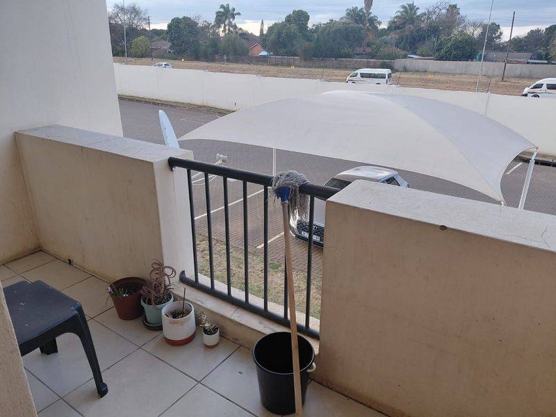 A functional balcony space featuring tiled flooring and a metal balustrade, overlooking a parking area with shade cloth structures.