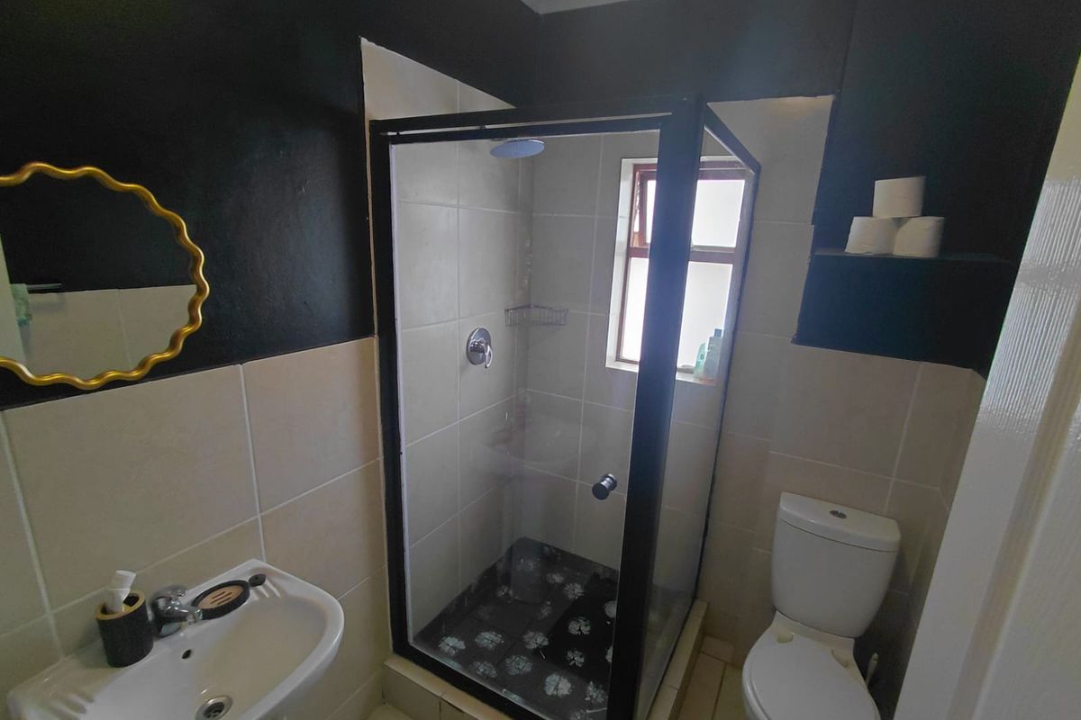 A compact bathroom featuring a shower enclosure, pedestal basin, and toilet, finished with neutral wall tiles and contrasting dark painted accents.