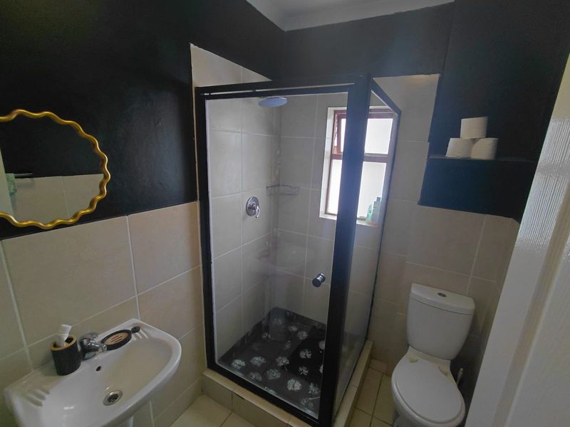 A compact bathroom featuring a shower enclosure, pedestal basin, and toilet, finished with neutral wall tiles and contrasting dark painted accents.
