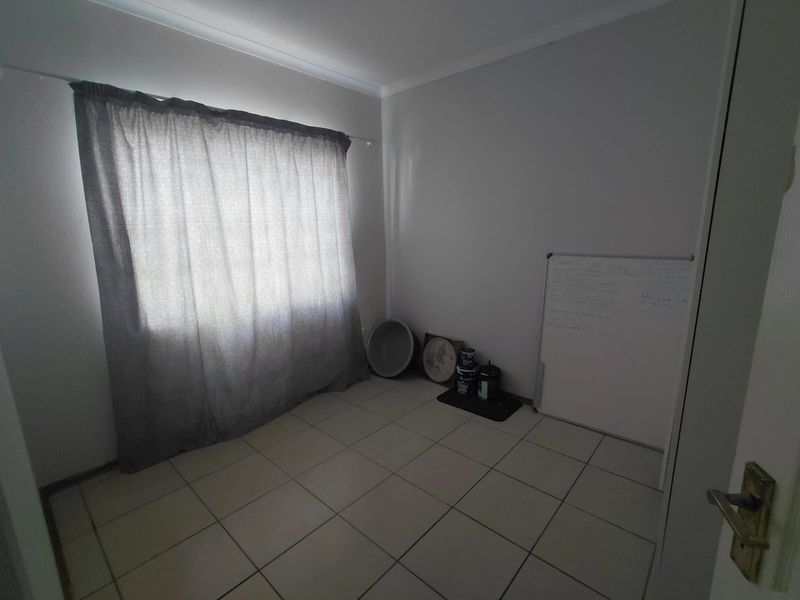 A vacant bedroom featuring neutral wall paint, tiled flooring, and a curtain rod, offering a blank canvas for personalization.
